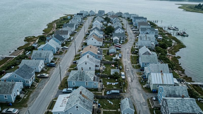 A coastal neighborhood of low houses seen from above, with water on two sides