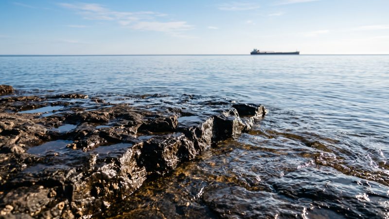 Wet basalt shelf rock at the edge of Lake Superior with a distant freighter on the horizon.