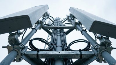 A rooftop cellular antenna array photographed tight from directly below, the flat panel antennas and their mounting brackets filling the frame against a pale overcast sky.